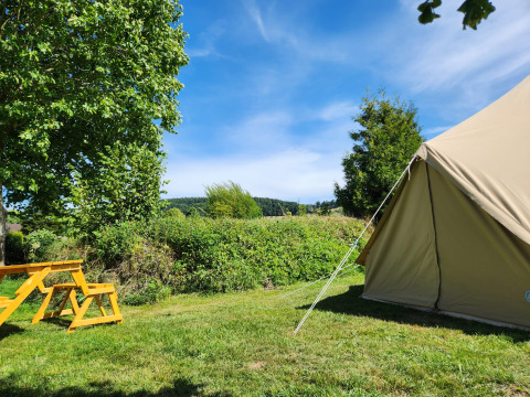 Safari-belltelt og gult picnicbord på Camp Diekirch i Luxembourg, omgivet af grønne træer og blå himmel.