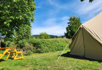 Tente safari et banc pique-nique jaune au Camp Diekirch au Luxembourg, entourés de verdure et ciel bleu.