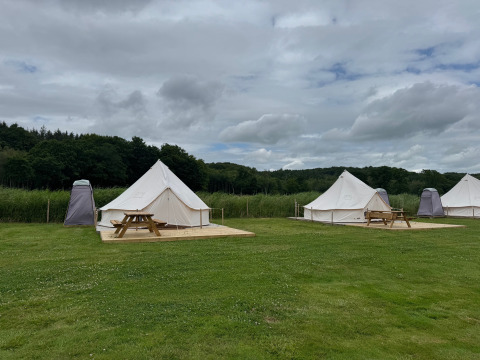 Tipi con terrazza in legno e tavoli da picnic al Rosenvold Strand Camping, Danimarca, in una giornata nuvolosa.
