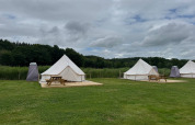 Tipi con terrazza in legno e tavoli da picnic al Rosenvold Strand Camping, Danimarca, in una giornata nuvolosa.