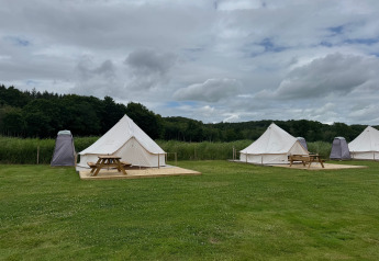 Tipi tenten met houten terras en picknicktafels bij Rosenvold Strand Camping, Denemarken, op een bewolkte dag.