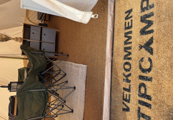 Entrada a una tienda tipi en Rosenvold Strand Camping, Dinamarca, con felpudo de bienvenida y sillas de camping.