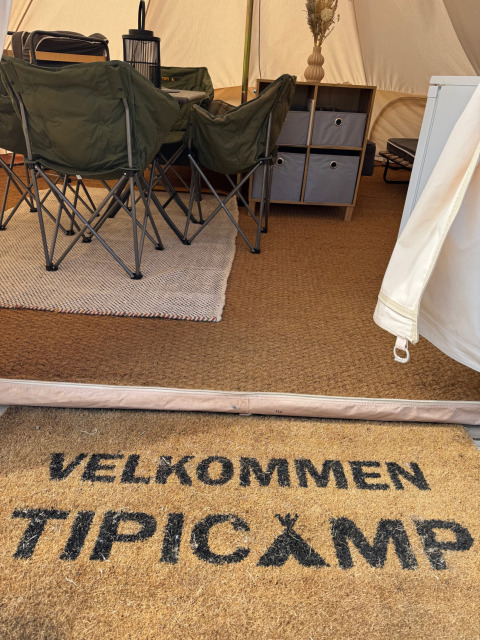 Entrée d’une tente tipi au Rosenvold Strand Camping au Danemark avec paillasson de bienvenue et chaises de camping.