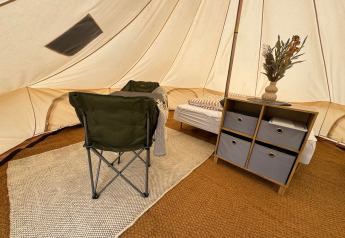 Intérieur d’une tente Tipi au Rosenvold Strand Camping avec chaise, lit, étagère et fleurs séchées.