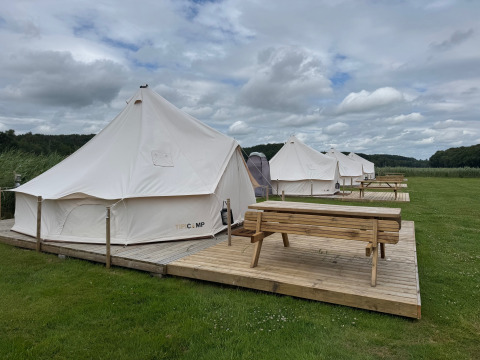 Række tipi-telte med træterrasse og bænke ved Rosenvold Strand Camping i Danmark under overskyet himmel.