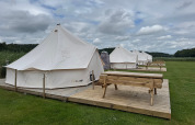 Rij van tipi-tenten met houten terrassen en banken op Rosenvold Strand Camping in Denemarken onder een bewolkte hemel.
