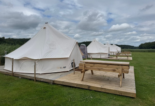 Rangée de tentes tipi avec terrasses en bois et bancs à Rosenvold Strand Camping, Danemark, sous ciel nuageux.