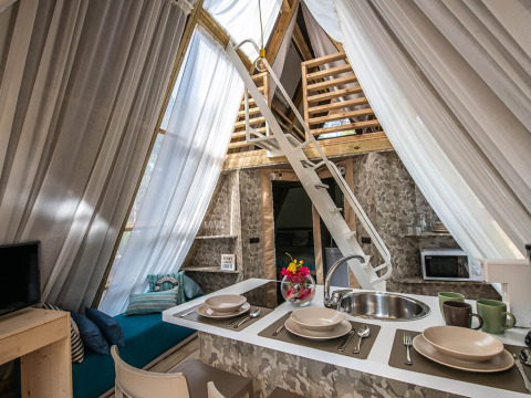 Cozy safari tent interior with a small kitchen, dining setup, loft ladder and sheer curtains for light.