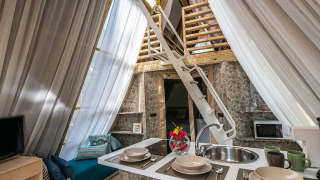 Knus interieur van safaritent met kitchenette, eethoek, trap naar mezzanine en lichtdoorlatende gordijnen.
