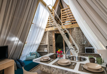 Interno accogliente di tenda safari con cucina, tavolo apparecchiato, scala per soppalco e tende chiare.