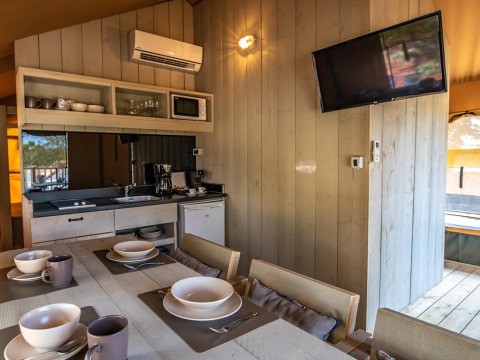 Modern glamping kitchen and dining area with tableware, air conditioning, and TV at Camping Arena One 99.