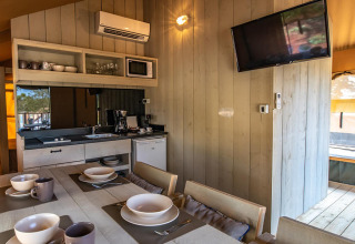 Modern glamping kitchen and dining area with tableware, air conditioning, and TV at Camping Arena One 99.