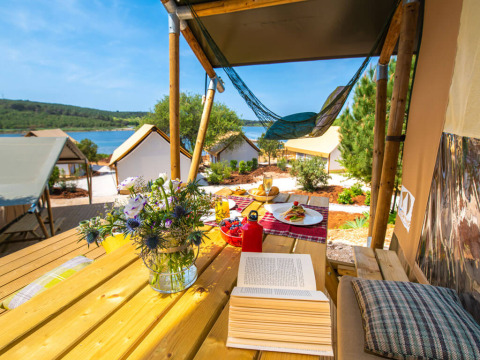 Zicht vanop het terras van een safaritent met bloemen, boek en eten bij het meer aan Arena One 99 Glamping, Kroatië.