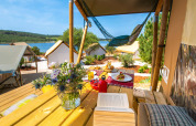 Udsigt fra en safariteltterrasse med blomster, bog, mad og sø i baggrunden på Arena One 99 Glamping, Kroatien.