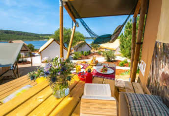 Vista dalla terrazza di una tenda safari con fiori, libro e cibo sul lago ad Arena One 99 Glamping, Croazia.