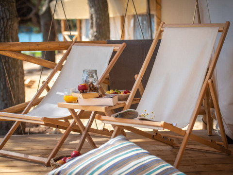 Due sedie a sdraio e un tavolino con snack e succo su una terrazza di una tenda safari in Croazia.