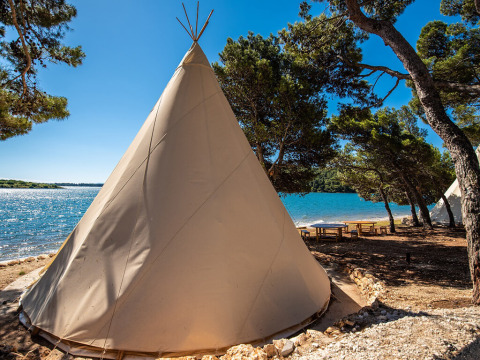 Large tipi near the lakeside surrounded by trees and picnic tables at Camping Arena One 99 Glamping, Istria, Croatia