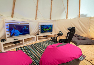 Area gaming in tenda con due TV, sedia da corsa Playseat, pouf colorati e console su pavimento in legno.