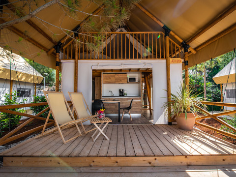 Glamping tent at Camping Arena One 99 in Istria, Croatia, featuring a wooden deck, lounge chairs and kitchenette.