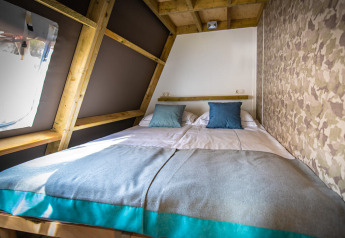 Cozy bed with blue pillows inside a safari tent, featuring wooden beams and camouflage wallpaper.