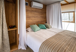 Moderne safaritent slaapkamer met tweepersoonsbed, houten accenten, witte gordijnen en airconditioning.