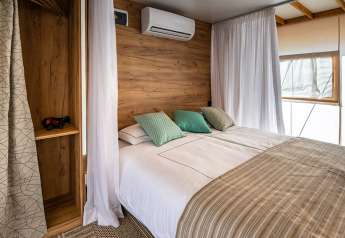 Modern safari tent bedroom with a double bed, wooden décor, white linens, curtains and air conditioning.