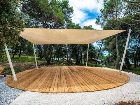 A circular wooden deck with sail canopy in a forested area at Camping Arena One 99 Glamping, Istria, Croatia.