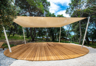 A circular wooden deck with sail canopy in a forested area at Camping Arena One 99 Glamping, Istria, Croatia.