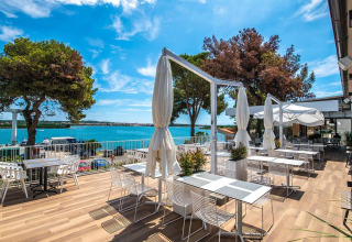 Udendørs terrasse med spiseborde og udsigt over havet og træer på Camping Arena One 99 Glamping i Istrien, Kroatien.