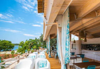 Outdoor-Restaurant mit Holzmöbeln und Blick aufs Wasser im Camping Arena One 99 Glamping, Istrien, Kroatien.