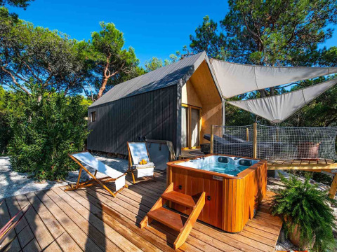 Luxury tent with hot tub and sun loungers on a wooden deck, surrounded by pine trees at Camping Arena One 99 Glamping.