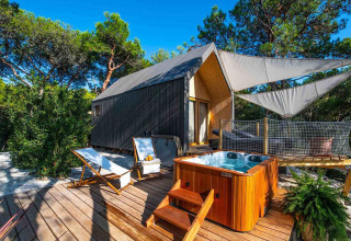 Luxury tent with hot tub and sun loungers on a wooden deck, surrounded by pine trees at Camping Arena One 99 Glamping.