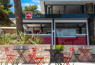 Zona caffè all'aperto al Camping Arena One 99 Glamping in Istria, Croazia, con sedie rosse e tavolini neri.
