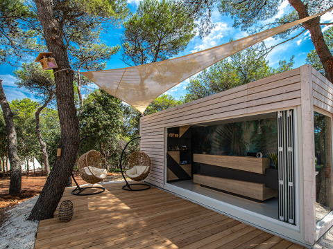 Lounge all’aperto moderna e reception al Camping Arena One 99 Glamping in Istria, Croazia, circondata da alberi.