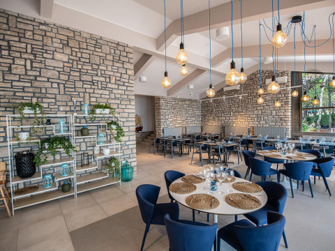 Modern restaurant with stone walls, blue chairs, and hanging lights at Camping Arena One 99 Glamping, Istria.