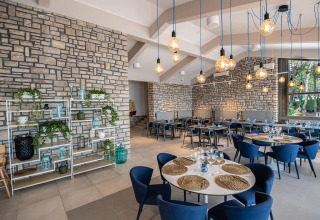 Restaurant moderne avec murs en pierre, chaises bleues et luminaires suspendus au Camping Arena One 99 Glamping, Istrie.