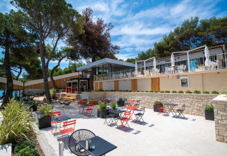 Outdoor terrace with tables and chairs among pine trees at Camping Arena One 99 Glamping in Istria, Croatia.