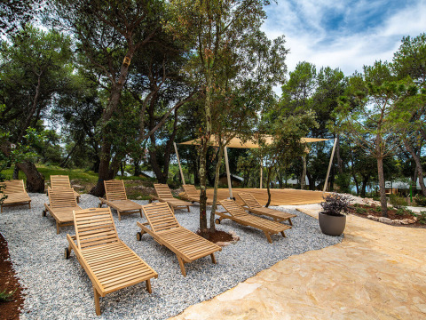Zona relax con lettini in legno all’ombra degli alberi presso Camping Arena One 99 Glamping in Istria, Croazia.