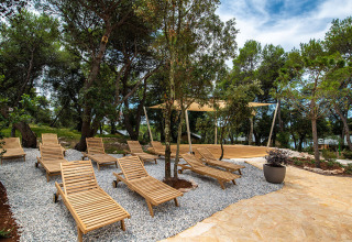 Zona relax con lettini in legno all’ombra degli alberi presso Camping Arena One 99 Glamping in Istria, Croazia.