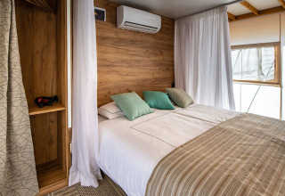 Camera accogliente in una tenda safari con letto matrimoniale, cuscini, armadio e aria condizionata.