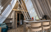 Interior of a safari tent featuring modern decor, small kitchen, lounge area, and a loft with sheer curtains.