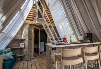 Interno di una tenda safari con arredamento moderno, cucina, area relax e soppalco sotto tende leggere.