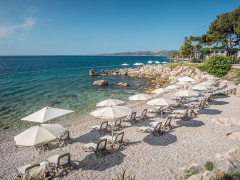 Sonnenliegen und Sonnenschirme am steinigen Strand von Valamar Camping Ježevac in Kroatiens Primorje-Gorski Kotar.