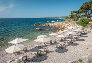 Lettini e ombrelloni sulla spiaggia di ciottoli al Valamar Camping Ježevac in Primorje-Gorski Kotar, Croazia.