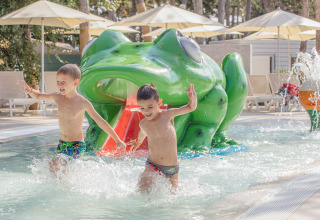 Zwei Kinder spielen im Kinderbecken vor einer großen Froschrutsche im Valamar Camping Ježevac, Kroatien.