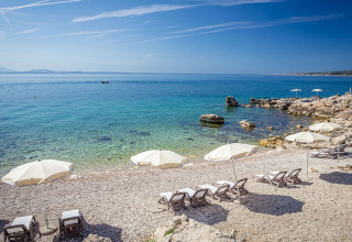 Kiezelstrand met ligbedden en witte parasols bij Valamar Camping Ježevac in Kroatië aan de kust.