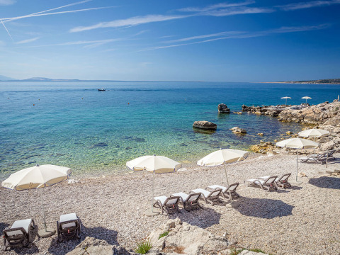 Kiesstrand mit Sonnenliegen und Sonnenschirmen am klaren Wasser in Valamar Camping Ježevac, Kroatien.