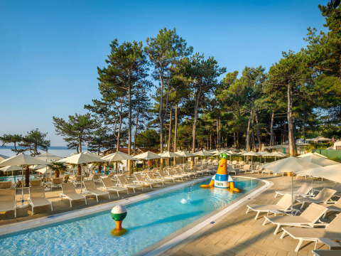 Piscina per bambini con giochi gonfiabili, lettini e ombrelloni tra pini a Valamar Camping Ježevac.