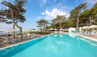 Outdoor pool with sun loungers, umbrellas, and pine trees at Valamar Camping Ježevac holiday park, Croatia