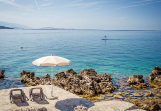 Sonnige Liegen und Sonnenschirm auf felsiger Küste bei Valamar Camping Ježevac, Kroatien mit ruhigem Meer.